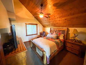 Bedroom featuring vaulted ceiling, wood ceiling, a ceiling fan, and dark colored carpet