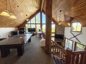 Recreation room featuring plenty of natural light, a ceiling fan, wooden ceiling, a stone fireplace, and high vaulted ceiling