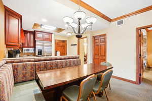 Dining area featuring a chandelier, light colored carpet, and ornamental molding