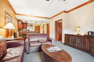 Carpeted living room featuring a chandelier, ornamental molding, and ceiling fan