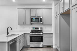 Kitchen with gray cabinets, stainless steel appliances, a peninsula, light countertops, and recessed lighting