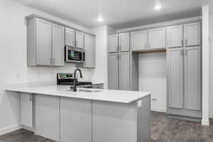 Kitchen with gray cabinets, a peninsula, stainless steel microwave, dark wood-type flooring, and light countertops