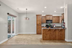 Kitchen with brown cabinets, black appliances, a peninsula, dark stone countertops, and recessed lighting