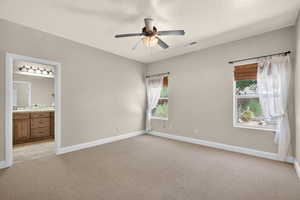 Unfurnished bedroom featuring light colored carpet, multiple windows, connected bathroom, and a ceiling fan