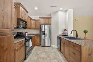 Kitchen with black appliances, a peninsula, brown cabinets, stone counters, and recessed lighting