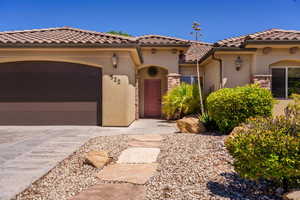 Mediterranean / spanish house with stucco siding, a garage, concrete driveway, a tile roof, and stone siding