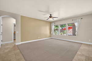 Unfurnished room featuring arched walkways, light tile patterned flooring, light carpet, and ceiling fan
