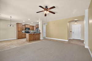 Kitchen featuring brown cabinets, arched walkways, open floor plan, recessed lighting, and pendant lighting