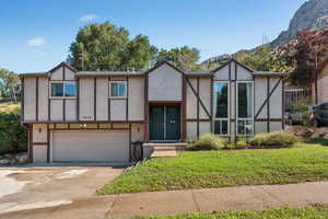 English style home with stucco siding, driveway, an attached garage, and a front lawn
