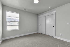 Unfurnished bedroom featuring light carpet, a textured ceiling, and a closet