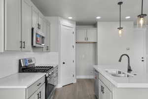 Kitchen featuring appliances with stainless steel finishes, wood finished floors, decorative light fixtures, light countertops, and a kitchen island with sink
