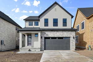 View of front of home with stone siding, a garage, driveway, and board and batten siding