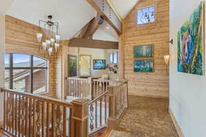 Hall featuring wood walls, an upstairs landing, high vaulted ceiling, a chandelier, and stone finish floors