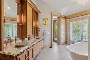 Bathroom featuring plenty of natural light, double vanity, a soaking tub, and lofted ceiling