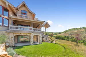 Rear view of property featuring stone siding, a yard, and a balcony