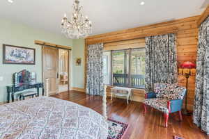 Bedroom with a barn door, wood-type flooring, wooden walls, a chandelier, and recessed lighting