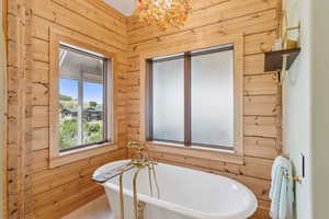 Full bath with a freestanding tub, a chandelier, and wood walls