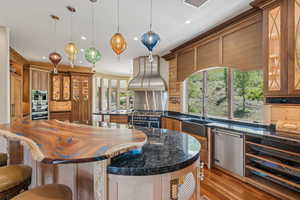Kitchen with a kitchen breakfast bar, stainless steel appliances, island exhaust hood, light wood-type flooring, and brown cabinetry