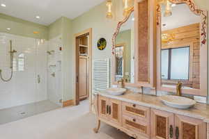 Full bath featuring a shower stall, double vanity, radiator, and a chandelier