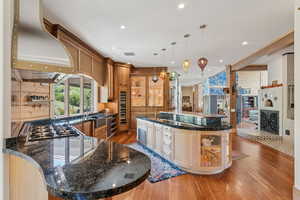 Kitchen featuring wood-type flooring, wall chimney exhaust hood, a spacious island, glass insert cabinets, and recessed lighting