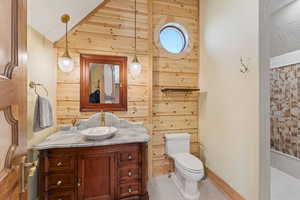 Full bath featuring vanity, a tile shower, wooden walls, and lofted ceiling