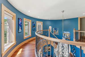 Hall with an upstairs landing, wood finished floors, and recessed lighting