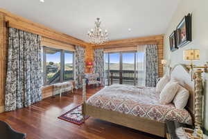 Bedroom featuring multiple windows, wood walls, wood finished floors, a chandelier, and access to outside