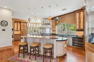 Kitchen featuring a kitchen breakfast bar, wood finished floors, a large island, ventilation hood, and pendant lighting