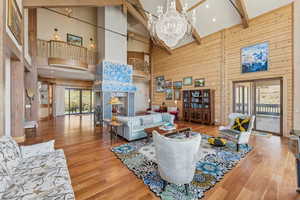 Living room with wooden walls, beam ceiling, plenty of natural light, a chandelier, and wood finished floors