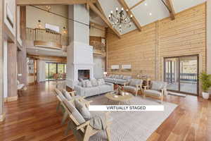 Living area featuring wood walls, a chandelier, a lit fireplace, wood finished floors, and lofted ceiling