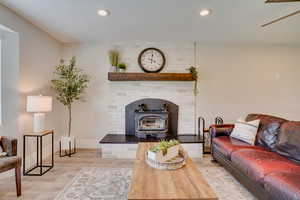 Living room with light wood finished floors, a textured ceiling, recessed lighting, ceiling fan, and a wood stove