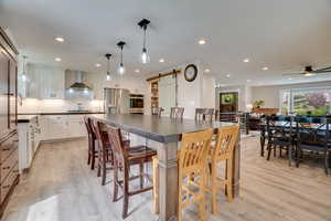 Kitchen featuring a barn door, dark countertops, wall chimney range hood, white cabinetry, and light wood finished floors