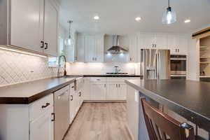 Kitchen with dark countertops, stainless steel appliances, light wood finished floors, pendant lighting, and white cabinets