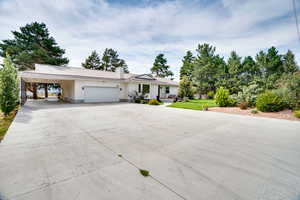 Ranch-style home with a metal roof, concrete driveway, a carport, a chimney, and an attached garage