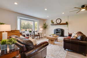 Living room featuring light wood finished floors, a textured ceiling, recessed lighting, ceiling fan, and a wood stove