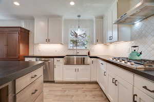 Kitchen with wall chimney range hood, decorative backsplash, appliances with stainless steel finishes, light wood-style floors, and pendant lighting