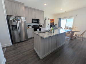 Kitchen with black appliances, a center island with sink, dark wood finished floors, recessed lighting, and light stone countertops