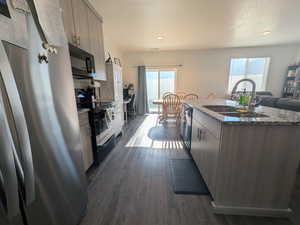 Kitchen with black appliances, an island with sink, dark wood-style flooring, stone counters, and modern cabinets