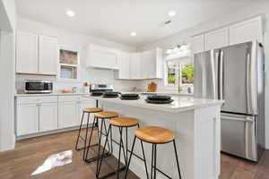 Kitchen with stainless steel appliances, white cabinetry, dark wood-style flooring, a kitchen bar, and recessed lighting
