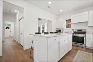 Kitchen featuring stainless steel range with gas stovetop, dark wood finished floors, recessed lighting, light countertops, and white cabinets