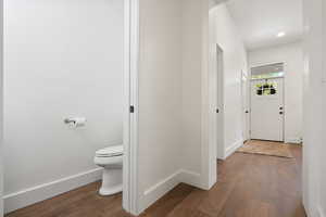 Hall with wood finished floors and baseboards and half bathroom.