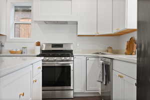 Kitchen featuring stainless steel appliances, light countertops, white cabinets, and dark wood finished floors