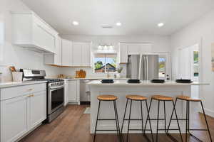 Kitchen featuring appliances with stainless steel finishes, a breakfast bar area, dark wood finished floors, white cabinetry, and recessed lighting