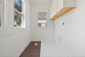 Laundry area featuring hookup for an electric dryer, cabinet space, and dark wood-style floors.  Built in sink for washing.