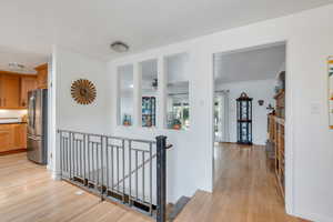 Hall with an upstairs landing, light wood finished floors, and ornamental molding