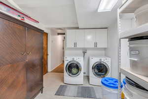 Laundry room featuring cabinet space, washer and clothes dryer, light tile patterned flooring, and a textured ceiling