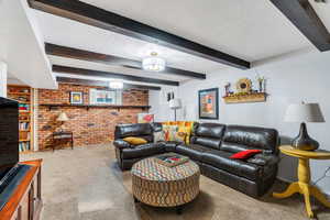 Carpeted living area with a textured ceiling, brick wall, and beamed ceiling