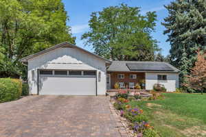 Single story home with board and batten siding, a front lawn, solar panels, and decorative driveway