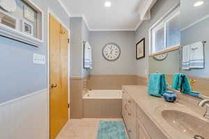 Bathroom featuring wainscoting, ornamental molding, a garden tub, vanity, and tile patterned flooring