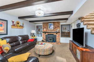 Living area with a textured ceiling, carpet flooring, beam ceiling, and a wood stove